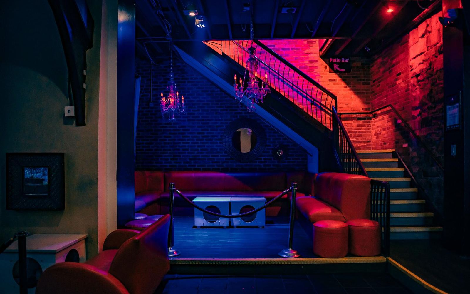 A red velvet lounge beneath a lit staircase and a small chandelier.