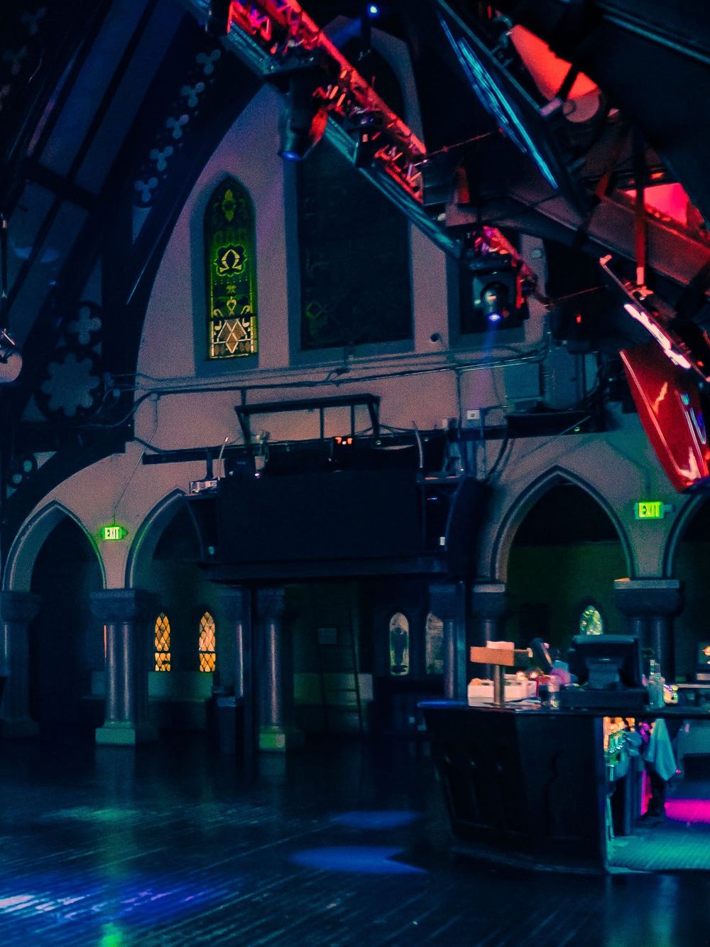 A stained glass window set high in a gothic wall above the club floor, lit in blue and red.